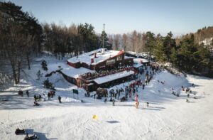 winter in pieria with a white snowy floor and a small wooden chalet and lots of guests