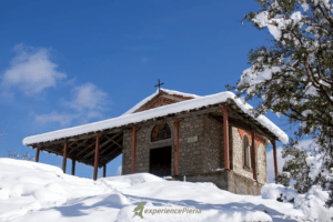 snowy white ground and Chapel of Prophet Elias in Litochoro on the top with a clear sky above.