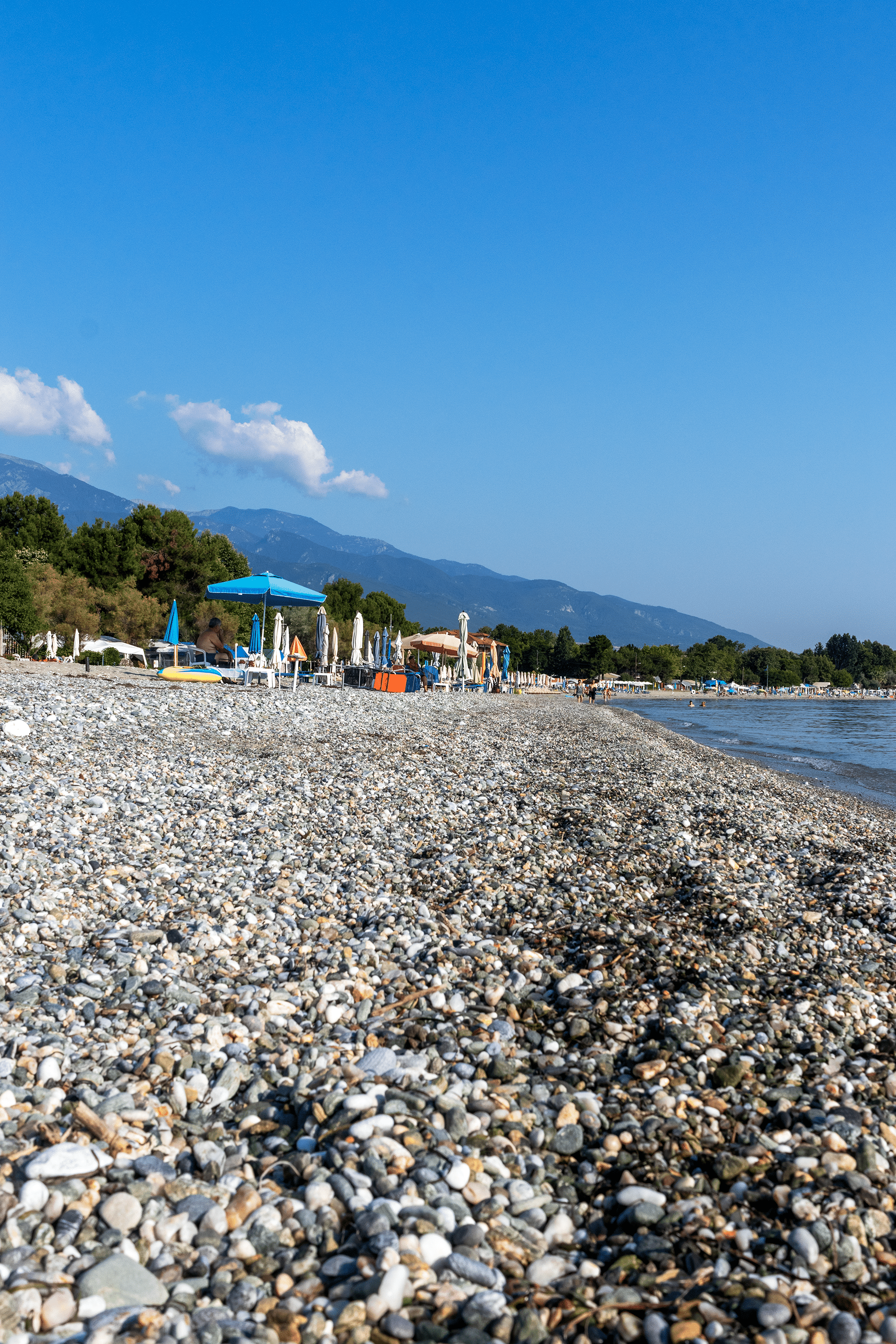 Sunbeds and closed umbrellas Infront of the Beach on the pebbles of Pnateleimon Beach, Pieria region, Greece.