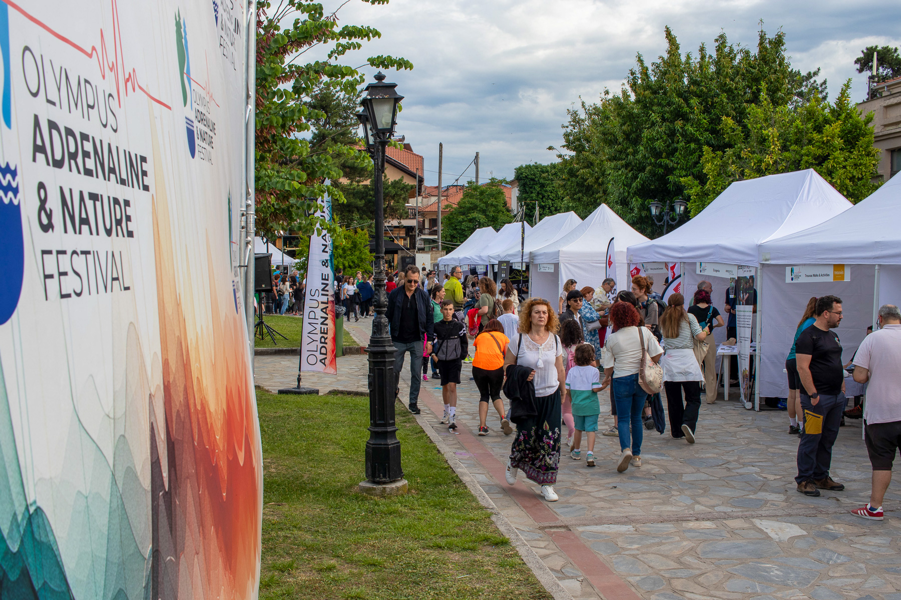 Crowd walking in Litochoro park under the Olympus Adrenaline & Nature Festival banner