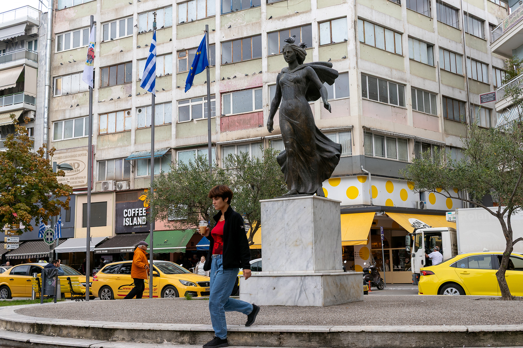 Anna walking in Plateia Eleftherias, Katerini Pieria Greece, holding coffee to go