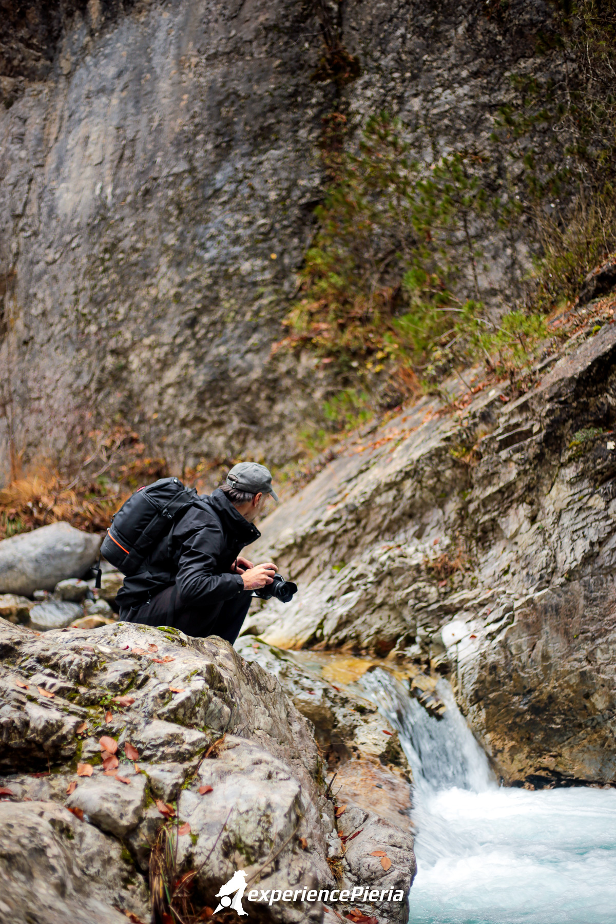 Giorgos Gizelis standing by the Enipeas river on Mount Olympus with a camera in hand, searching for the best waterfall frame