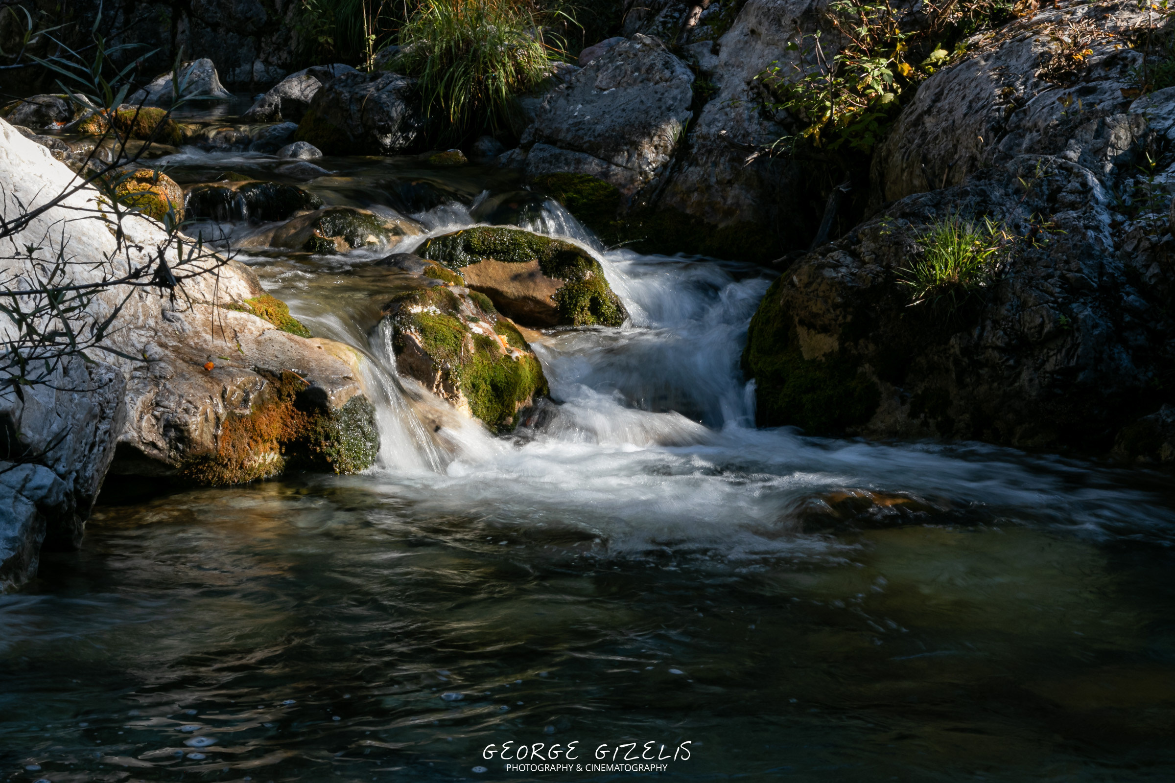 Small cascades flowing over rocks in the Enipeas River beneath a wooden bridge on Mount Olympus.